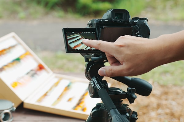 Image of a camera set up at an outdoor shoot, with a man’s finger touching the camera’s monitor