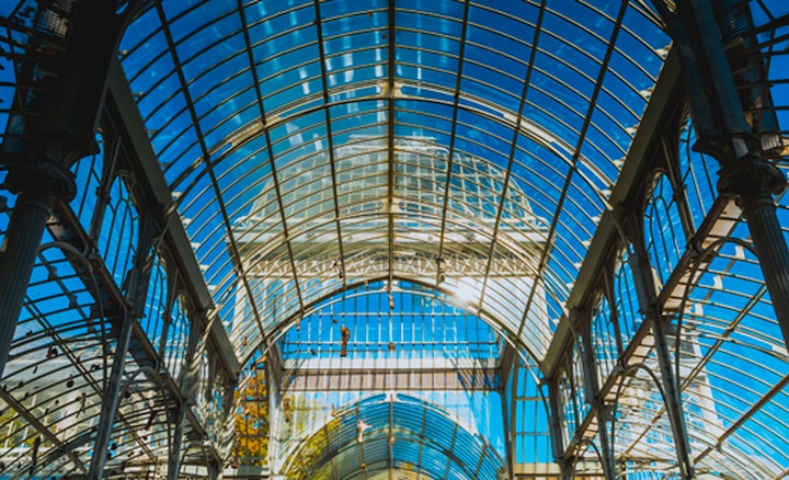 Interior shot of a glass building showing detail in architecture and blue sky beyond