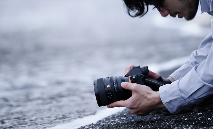 Un photographe est à genoux au bord de l’eau, prenant des photos sous un angle suggérant qu’il est dans la mer.