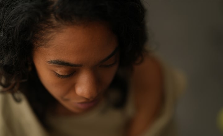 Portrait vu du dessus représentant une femme noire aux longs cils qui regarde vers le bas dans un intérieur à l’éclairage tamisé.