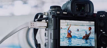 Image d’utilisation de l’appareil photo monté sur un trépied et connecté à un câble de réseau local, capturant un match de water-polo avec des images diffusées en temps réel sur un moniteur LCD