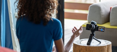 Image d’une femme en train d’effectuer une diffusion en direct à l’aide de l’appareil photo, sur lequel est fixée une poignée utilisée comme trépied sur une table basse