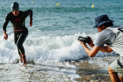 Image d’utilisation d’un homme tenant l’appareil photo pour filmer un triathlète courant hors de la mer