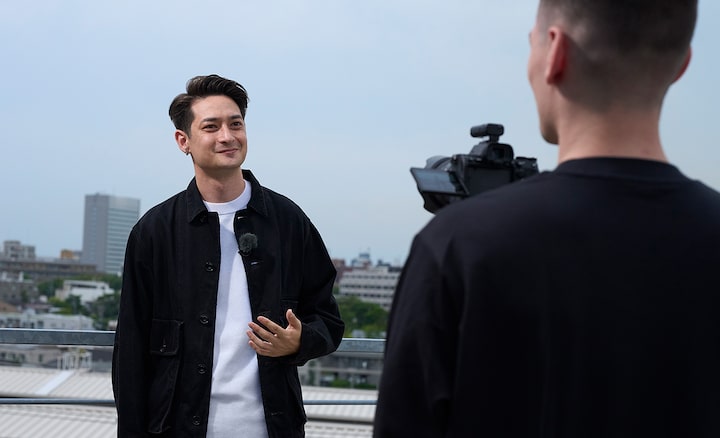 Image d’utilisation montrant un homme tenant à la main un appareil photo, en train de tourner des images d’un autre homme équipé d’un microphone ECM-L1 en extérieur