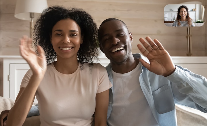 Image of couple in living room waving at a friend during video chat