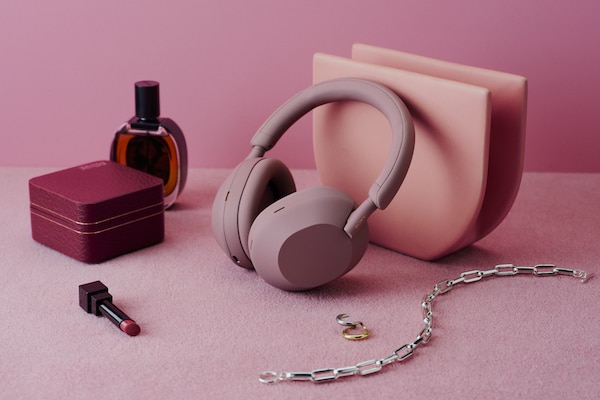 Le casque sans fil WH-1000XM5 couleur rose fumé posé sur un tapis rose à côté d’accessoires de beauté.