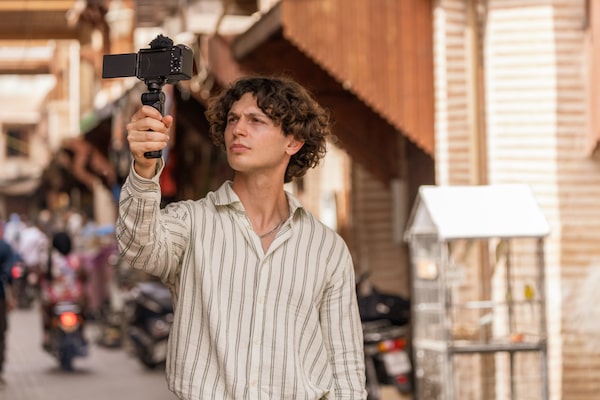 Image d’utilisation montrant un homme qui se filme en train de marcher dans la rue, en tenant dans sa main droite une poignée fixée à l’appareil photo