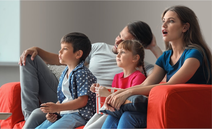 Man and woman with two children on sofa watching TV