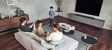 Family enjoying music in living room with TV and HT-A7000 soundbar on a marble cabinet