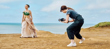 Image d’utilisation montrant une femme tenant un appareil photo à la main et capturant une autre femme en costume d’époque avec le bord de mer en arrière-plan