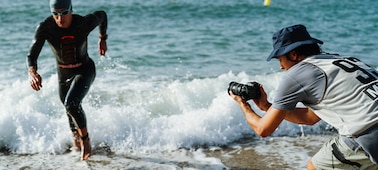 Image d’utilisation d’un homme tenant l’appareil photo pour filmer un triathlète courant hors de la mer