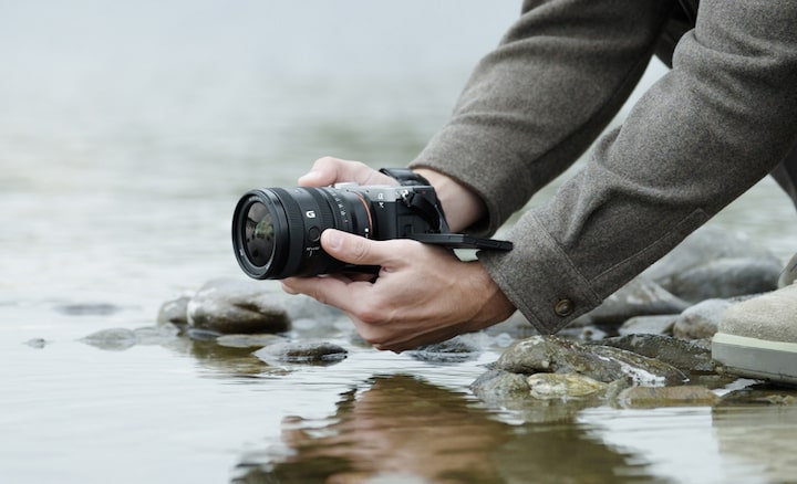 Image d’un utilisateur tenant le α7CII muni du FE 24-50 mm F2.8 G près de la surface d’une rivière. Il photographie en position basse.