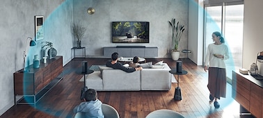 A family watching TV in a large living space. A blue dome illustrates the wide listening area of 360 Spatial Sound.