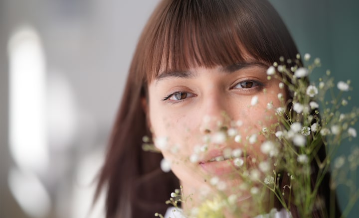 Portrait photo d’une femme blanche avec une frange et des cheveux lâchés, faisant face directement à l’appareil photo, avec un superbe effet bokeh créé par la présence de gypsophiles devant son visage.