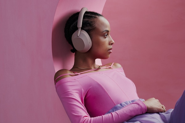 Photo promotionnelle d’une fille appuyée contre un mur rose, portant son casque sans fil WH-1000XM5.